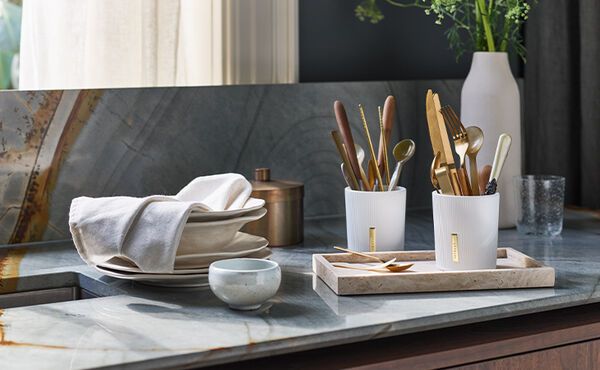 Upcycled Rituals candle holders used to store cutlery, styled on a marble kitchen countertop with plates and linen.